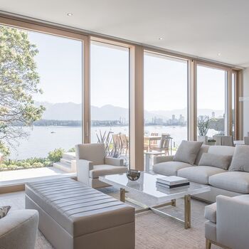 Blick aus hellem Wohnraum auf Terrasse und See durch UNILUX Holz-Alu Hebe-Schiebeanlage