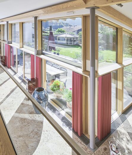 Großer heller Wohnraum mit Blick auf Ecke UNILUX FineLine Pfosten-Riegel-Fassade aus Holz und Alu