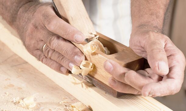 Schreiner bearbeitet Holzrahmen mit Hobel