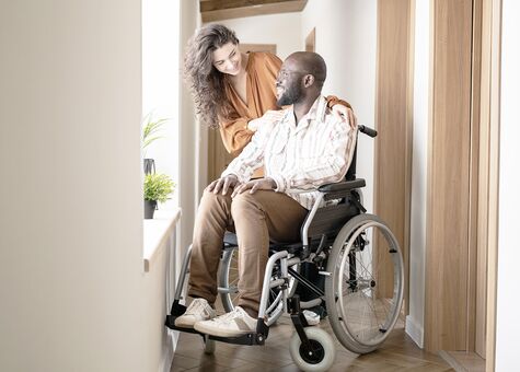 Junger Mann im Rollstuhl vor Fenster im Hausflur mit Partnerin