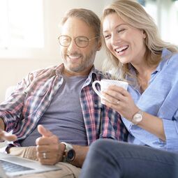Mann und Frau sitzen mit Kaffee und Laptop auf Couch und planen Holz Meisterfenster Denkmal