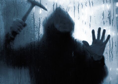 Einbrecher mit Hammer hinter Glasscheibe