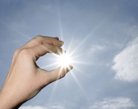 Hand hält Sonne zwischen Fingern Symbolbild