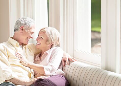 Best-Ager-Paar sitzt auf Sofa vor Kunststofffenster