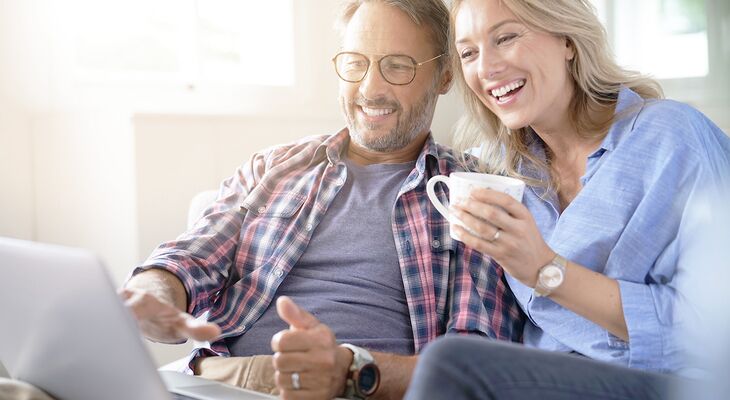 Mann und Frau sitzen mit Kaffee und Laptop auf Couch und planen Holz Meisterfenster Denkmal