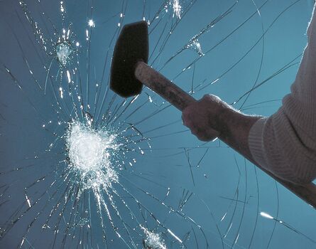Mann mit Vorschaghammer vor zerstörter Glasscheibe