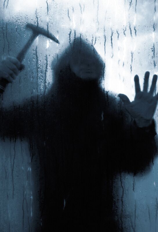 Einbrecher mit Hammer hinter Glasscheibe