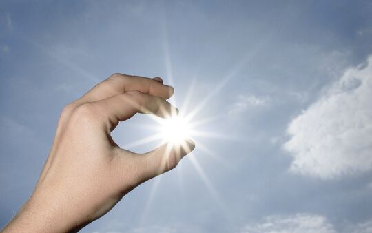 Hand hält Sonne zwischen Fingern Symbolbild